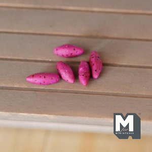 May include: Six miniature pink sweet potatoes, made of wood, with a textured surface. The sweet potatoes are arranged in a semi-circle on a wooden surface.