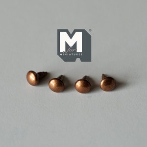 May include: Four copper-coloured metal tacks or nail heads with a rounded top and a small shank. The tacks are arranged in a row on a white surface. The image includes the logo "M for Miniatures".