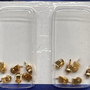 May include: Two clear plastic containers filled with small gold-coloured metal pulleys. The pulleys have a small metal hook on the top and a small wheel on the bottom.