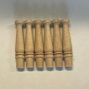 May include: Seven wooden spindles, each with a rounded top and a slightly flared base, are arranged in a row. The spindles are a light brown color and have a smooth finish.