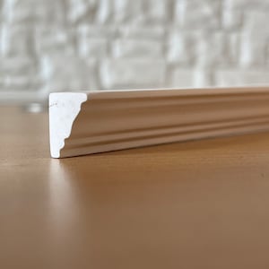 May include: White painted molding with a decorative edge. The molding is made of a smooth, hard material and has a slightly textured surface.