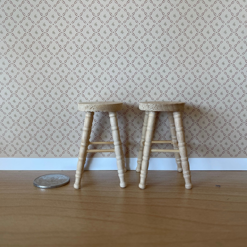 May include: Two wooden stools with a simple design, each with four legs and a single crossbar. The stools are light brown in colour and are sitting on a wooden floor.