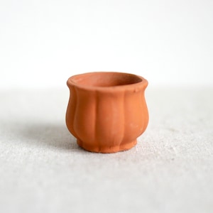 May include: A small terracotta pot with a fluted design. The pot is empty and has a light brown color.