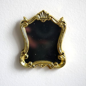 May include: A gold-colored ornate mirror with a black reflective surface. The mirror has a decorative frame with intricate details.