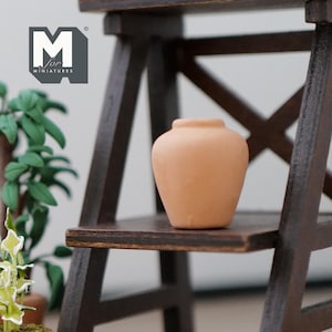 May include: A small terracotta pot sits on a wooden shelf. The pot is round and has a slightly flared lip. The shelf is part of a wooden ladder.
