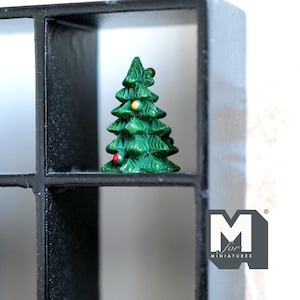Könnte beinhalten: Ein grüner Miniatur-Weihnachtsbaum mit roten und gelben Ornamenten. Der Baum wird in einem schwarzen, gitterartigen Regal ausgestellt. Das Logo "M for MINIATURES" ist unten rechts sichtbar.
