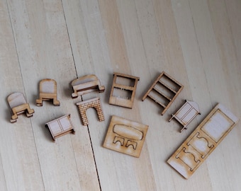 Könnte beinhalten: Eine Sammlung von Miniatur-Möbel-Ausschnitten aus Holz, darunter Stühle, ein Kamin, ein Bücherregal, ein Tisch und ein Schrank. Diese flachen, lasergeschnittenen Teile haben eine hellbraune Holzmaserung und sind verstreut angeordnet.