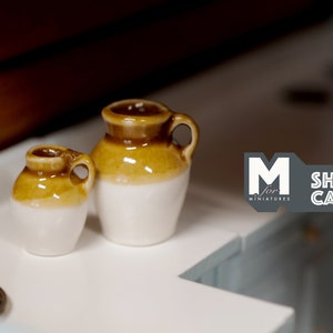 Peut inclure: Deux cruches miniatures en céramique brun et blanc avec des anses. La plus grande cruche mesure environ 5 cm de haut et la plus petite environ 4 cm de haut.
