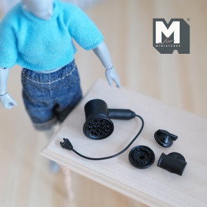 May include: A black miniature hairdryer with a cord and three attachments. The hairdryer has a black plastic body and a silver grill. The attachments are a round nozzle, a concentrator nozzle, and a diffuser nozzle.