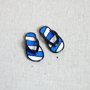 Op de afbeelding: Een paar blauwe en witte slippers met zwarte bandjes.