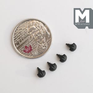 May include: Four small black plastic fasteners with pointed tips and rounded, textured heads, arranged in a diagonal line next to a silver 25-cent coin for scale. The coin features a portrait and a red maple leaf with the text 1812.
