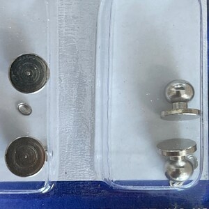 May include: Two sets of silver-toned metal knobs with a round base and a round top. The knobs are packaged in a clear plastic container.