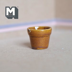 May include: A small, brown terracotta flower pot with a drainage hole. The pot is made of ceramic and has a rustic, earthy look.