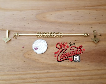 May include: Gold metal curtain rod with finials and rings. The rod is approximately the size of a Canadian one dollar coin.
