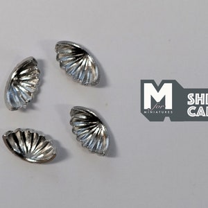 May include: Four silver, scallop-shaped, decorative embellishments.  These small, detailed pieces are perfect for adding a touch of elegance to crafts and miniature projects.