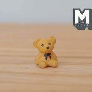May include: A small, brown teddy bear with a black bow tie sits on a wooden surface.
