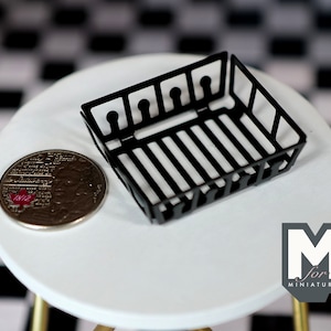May include: Black metal wire basket with a rectangular shape. The basket is sitting on a white surface with a black and white checkered pattern in the background.