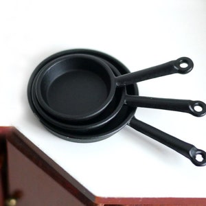 May include: Three black miniature frying pans with handles stacked on top of each other.