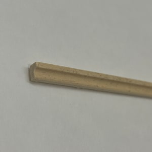 Könnte beinhalten: Nahaufnahme einer hellbraunen Holzleiste mit leicht abgerundeter Kante. Die Leiste ist etwa 30 cm lang und hat ein schlichtes, klassisches Design.