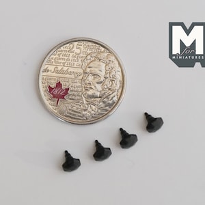 May include: Four black plastic furniture feet with a hexagonal shape. The feet are approximately the size of a Canadian 25-cent coin.