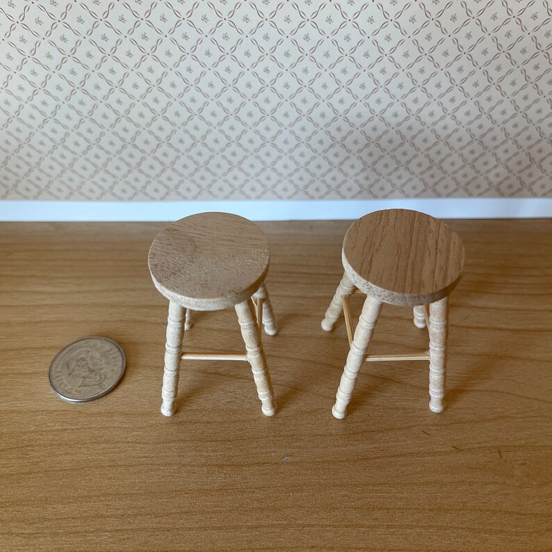 May include: Two wooden stools with a simple design. The stools are made of light brown wood and have a round seat. The stools are sitting on a wooden floor.