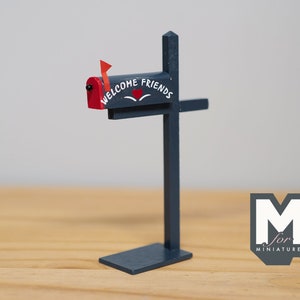 Pode incluir: Uma caixa de correio em miniatura azul escuro com uma bandeira vermelha e as palavras "WELCOME FRIENDS" pintadas na frente. A caixa de correio é montada em um poste correspondente. Um coração está entre as palavras.