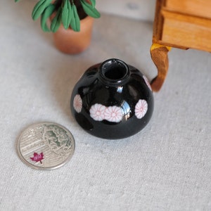 May include: A small black vase with a white and pink floral design. The vase is sitting on a light gray surface.