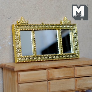 May include: Gold-toned, ornate, triple-paneled mirror with a decorative rope-like border. The mirror is mounted on a wooden dresser with multiple drawers.