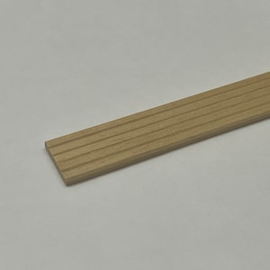 Può includere: Una striscia di legno marrone chiaro con una superficie scanalata. La striscia è lunga circa 30 cm e larga 2,5 cm.