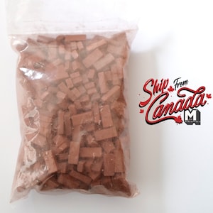 Puede incluir: Una bolsa de plástico transparente llena de pequeñas piezas de ladrillo rectangulares marrones. La bolsa está sellada y lista para ser utilizada para la construcción de modelos u otros proyectos de manualidades.