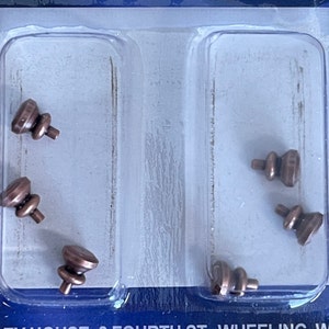 May include: Six small, brown, metal, decorative finials in a clear plastic package. The finials have a rounded top and a small, pointed base.