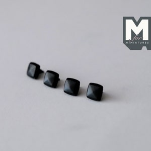 以下が含まれることがあります： 先端が尖ったピラミッド型の黒い正方形のスタッドが4つ。スタッドは白い表面に一列に並んでいます。