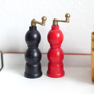 May include: Two small wooden salt and pepper shakers. The pepper shaker is black with a brass top and the salt shaker is red with a brass top.