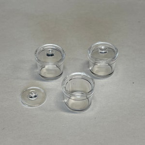 以下が含まれることがあります： ふた付きの透明なプラスチック容器が3つと、容器から分離したふたが1つ。容器は円筒形で、滑らかで透明な仕上げになっています。