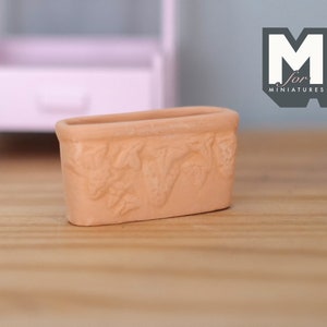 May include: A terracotta planter with a decorative leaf design. The planter is approximately 3 inches long and 1.5 inches wide.