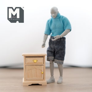 Peut inclure: Une petite table de chevet en bois avec un tiroir et une porte. Le tiroir a une poign&eacute;e dor&eacute;e et la porte a une poign&eacute;e dor&eacute;e. La table de chevet est en bois clair et a une finition naturelle.