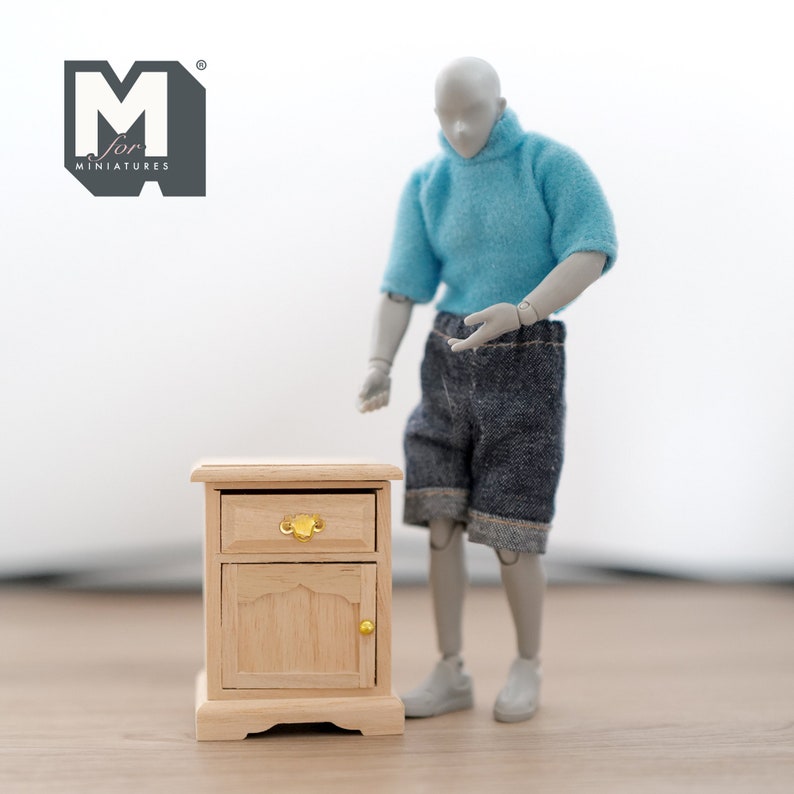 Peut inclure: Une petite table de chevet en bois avec un tiroir et une porte. Le tiroir a une poign&eacute;e dor&eacute;e et la porte a une poign&eacute;e dor&eacute;e. La table de chevet est en bois clair et a une finition naturelle.