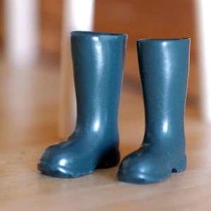 Op de afbeelding: Een paar kleine, teal-kleurige regenlaarzen. De laarzen zijn gemaakt van een glanzend materiaal en hebben een klassiek ontwerp, met een ronde neus en een hoogte tot halverwege de kuit. De laarzen staan op een houten oppervlak.