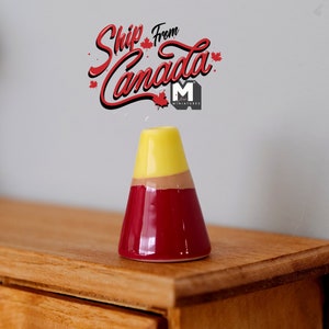 Könnte beinhalten: Eine kleine, farbenfrohe Keramikvase mit konischer Form. Die Oberseite ist gelb, geht in ein braunes Band über und hat dann einen tiefroten Sockel. Die Vase steht auf einer Holzoberfläche.