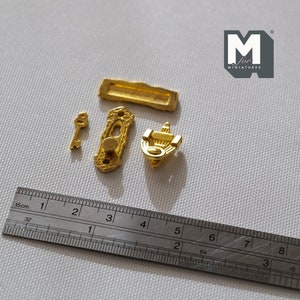 Könnte beinhalten: Ein Satz Miniatur-Türbeschläge in Goldton, bestehend aus einem Türklopfer, einem Türgriff, einer Schlüssellochabdeckung und einem Schlüssel. Die Beschläge sind neben einem Lineal abgebildet, das 8 cm misst.
