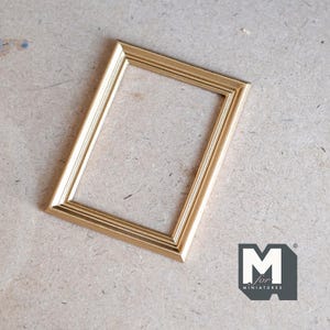 Könnte beinhalten: Ein goldfarbener Bilderrahmen mit einem einfachen, rechteckigen Design. Der Rahmen ist aus Holz und hat eine glatte Oberfläche.