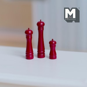 Peut inclure: Trois petits moulins à poivre rouges de différentes hauteurs. Les moulins sont cylindriques avec un dessus arrondi et un design nervuré. Le logo "M for miniatures" est dans le coin supérieur droit.