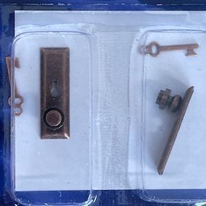 May include: A set of miniature door hardware in a copper finish. The set includes a door knob, a door handle, and a key.