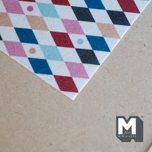 May include: A close-up of a fabric with a harlequin pattern. The design features diamond shapes in red, pink, blue, black, and tan on a white background. Small dots of matching colours are scattered across the design.