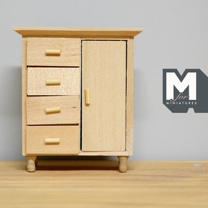 May include: A wooden miniature dresser with four drawers and a single door. The dresser has a light wood finish and simple wooden knobs. The dresser is sitting on a wooden surface.