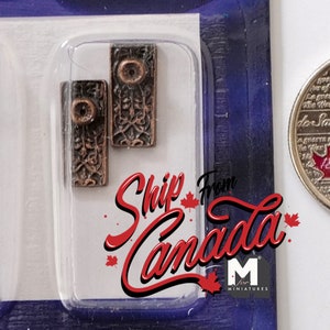 Könnte beinhalten: Vier Miniatur-Türbeschläge aus Metall in einer Plastikverpackung mit einer kanadischen 25-Cent-Münze als Größenvergleich. Die Beschläge sind dunkelbraun und haben ein dekoratives Design.