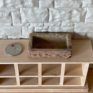 May include: A small, rectangular, decorative planter made of a light brown material with red and white accents. The planter is empty and has a rough, textured surface.