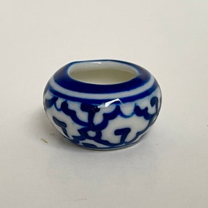 May include: A small, white ceramic pot with a blue and white floral design. The pot is round and has a wide opening.