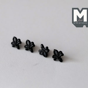 May include: Five black plastic fleur-de-lis embellishments. These are small, decorative pieces that can be used to add a touch of elegance to crafts and projects.