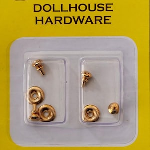 Op de afbeelding: Verpakking met poppenhuis hardware, inclusief goudkleurige knoppen en decoratieve ringen. De verpakking staat op een gele achtergrond, met de woorden "DOLLHOUSE HARDWARE" bovenaan gedrukt.